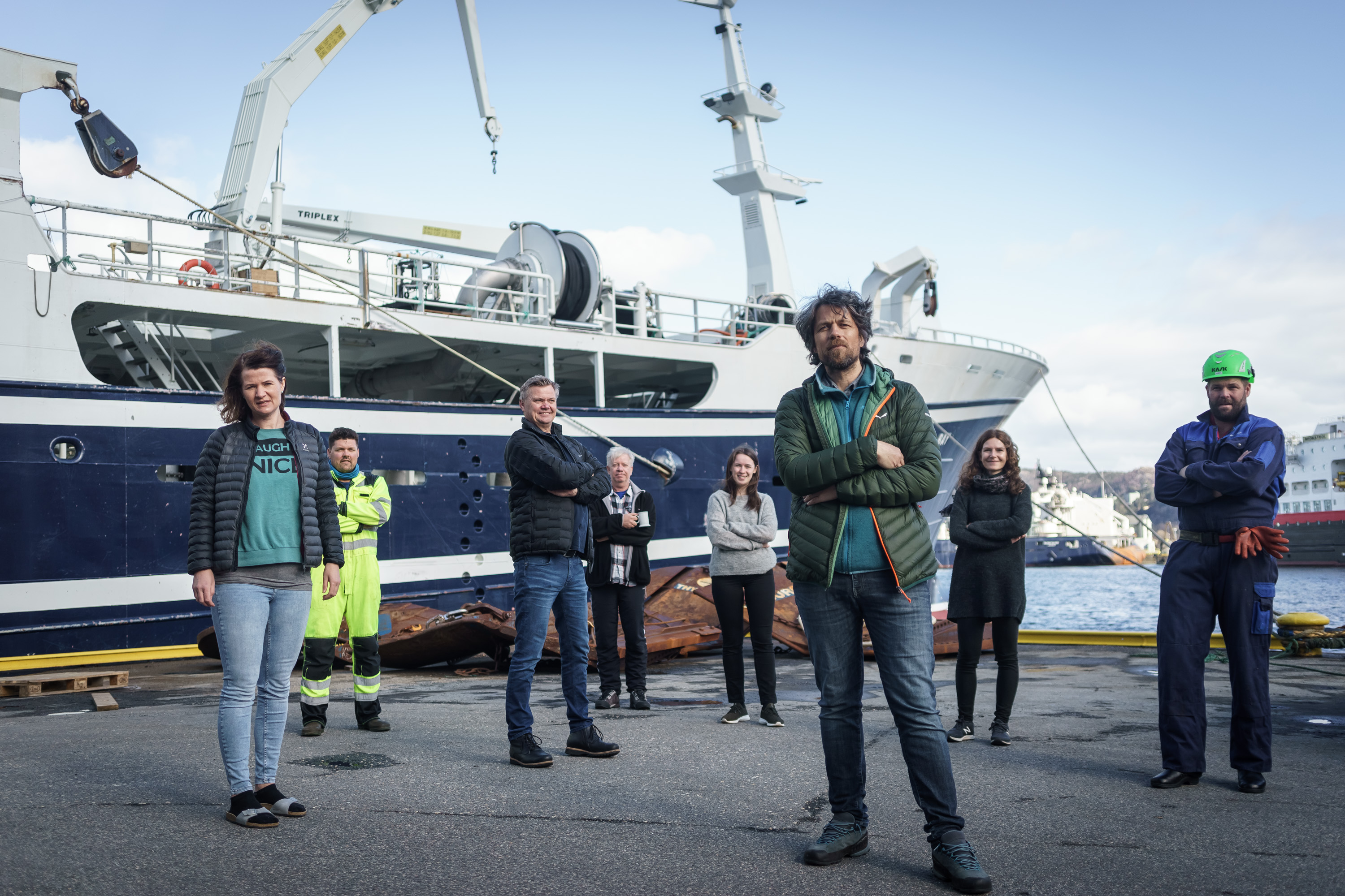 bilde av en rekke folk som står på kaien foran en fiskebåt