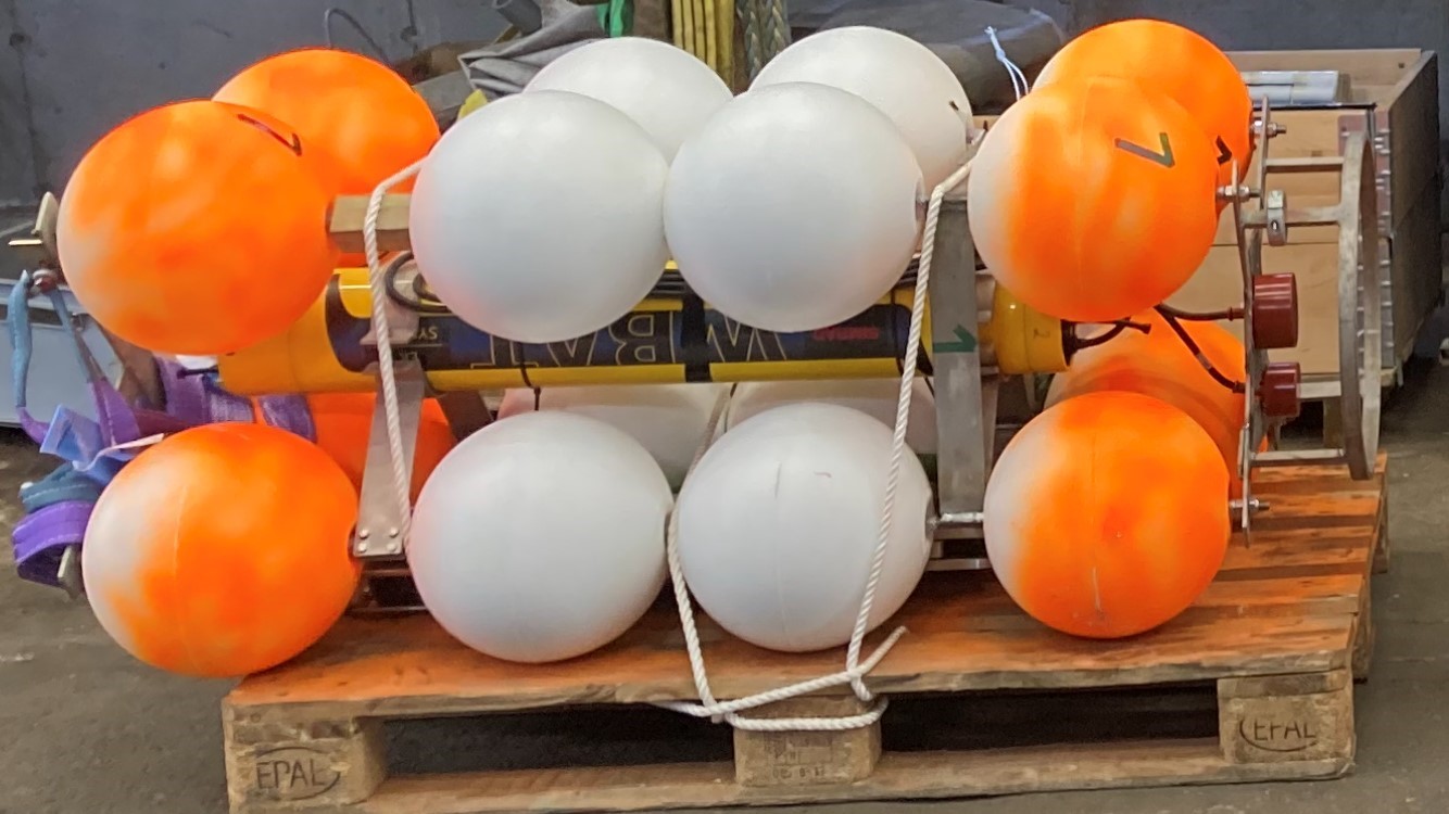 Picture of the WBAT setup when being docked on a transport “palle”. It shows its 16 buoys lined in four rows of four surrounding the steel frame holding the WBAT. Two transducers are fitted to the top of the frame.